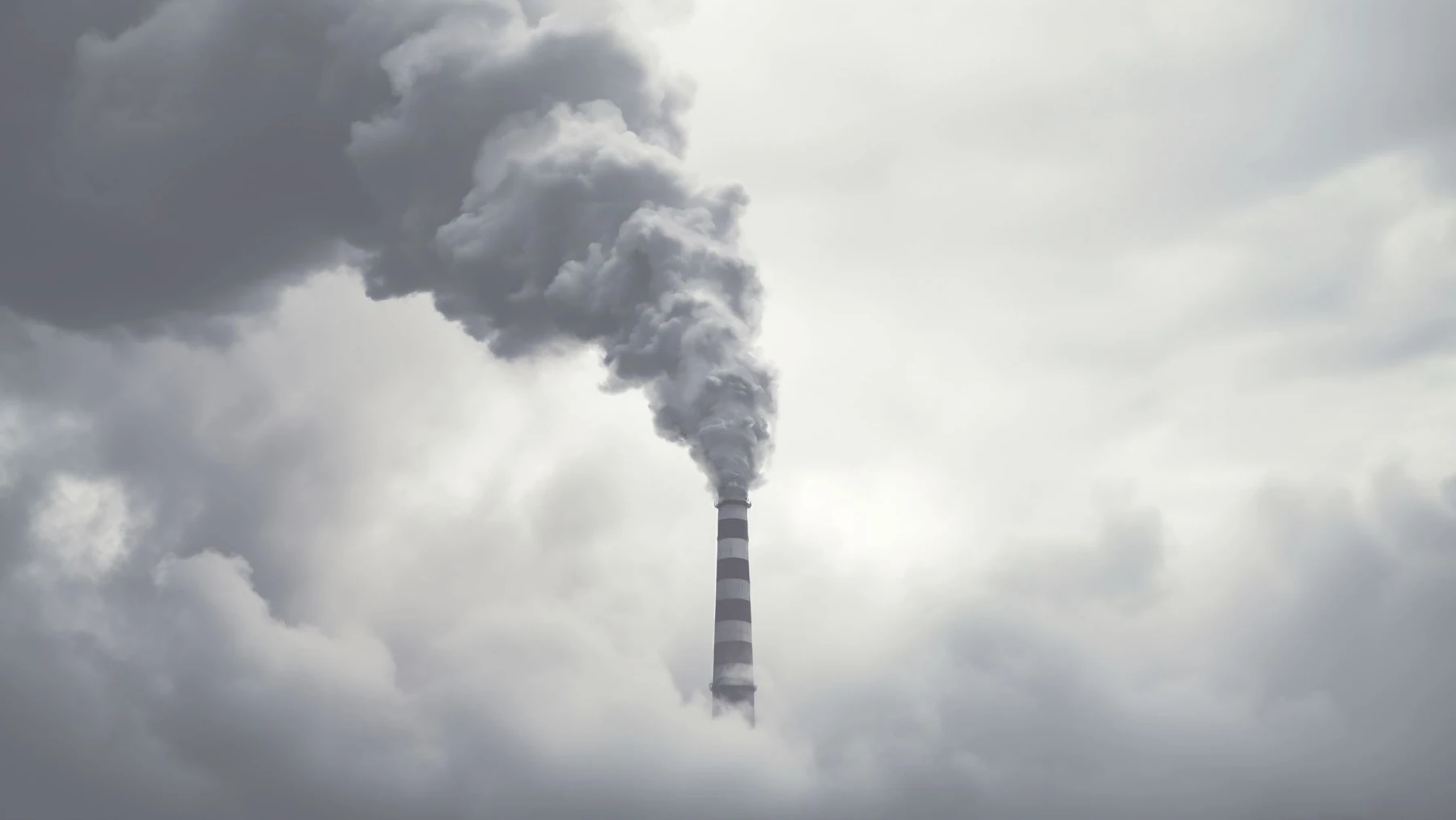 An industrial stack releases a visible plume into a cloudy sky.